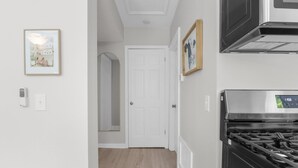 A hallway with a white door, a framed picture, a thermostat, and a stove. - Elegant 1 Bed Steps to Metra & Dining in Lake Forest! (Lake Forest)