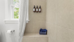 A bathroom with a toilet paper holder, a towel rack with bottles, and a blue towel basket.