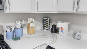 A kitchen with white cabinets, a coffee maker, and utensils in holders.