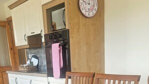 Ein Esstisch mit Platzsets und Stühlen, eine Uhr an der Wand sowie eine Küchenzeile mit Schränken und einem Backofen.