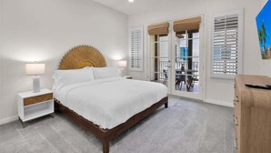 Ein Schlafzimmer mit Bett, Nachttisch, Lampe und Blick ins Freie durch eine Tür.