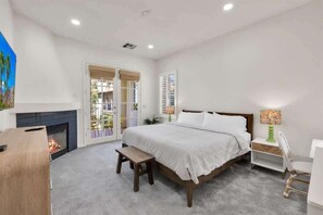 Un dormitorio con cama, un banco, un escritorio, una silla, chimenea y vistas a través de un ventanal.