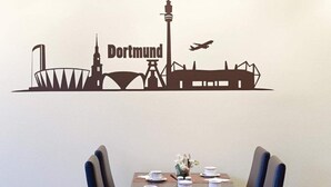 A wall decal of a city skyline with the word 'Dortmund' and a dining table with chairs and a vase of flowers. - 1 Person Holiday Park Home in Dortmund (Dortmund)