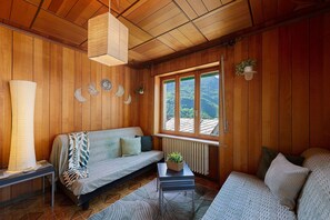 Habitació amb panells de fusta, un sofà, una taula petita amb una planta i una finestra amb vista a l'exterior.