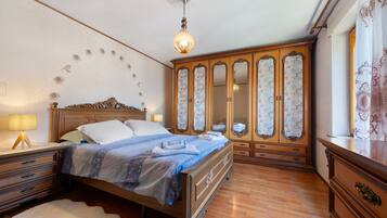 Ein Schlafzimmer mit einem hölzernen Bett, einem Nachttisch, einer Kommode und einem großen Spiegel mit floralem Dekor.