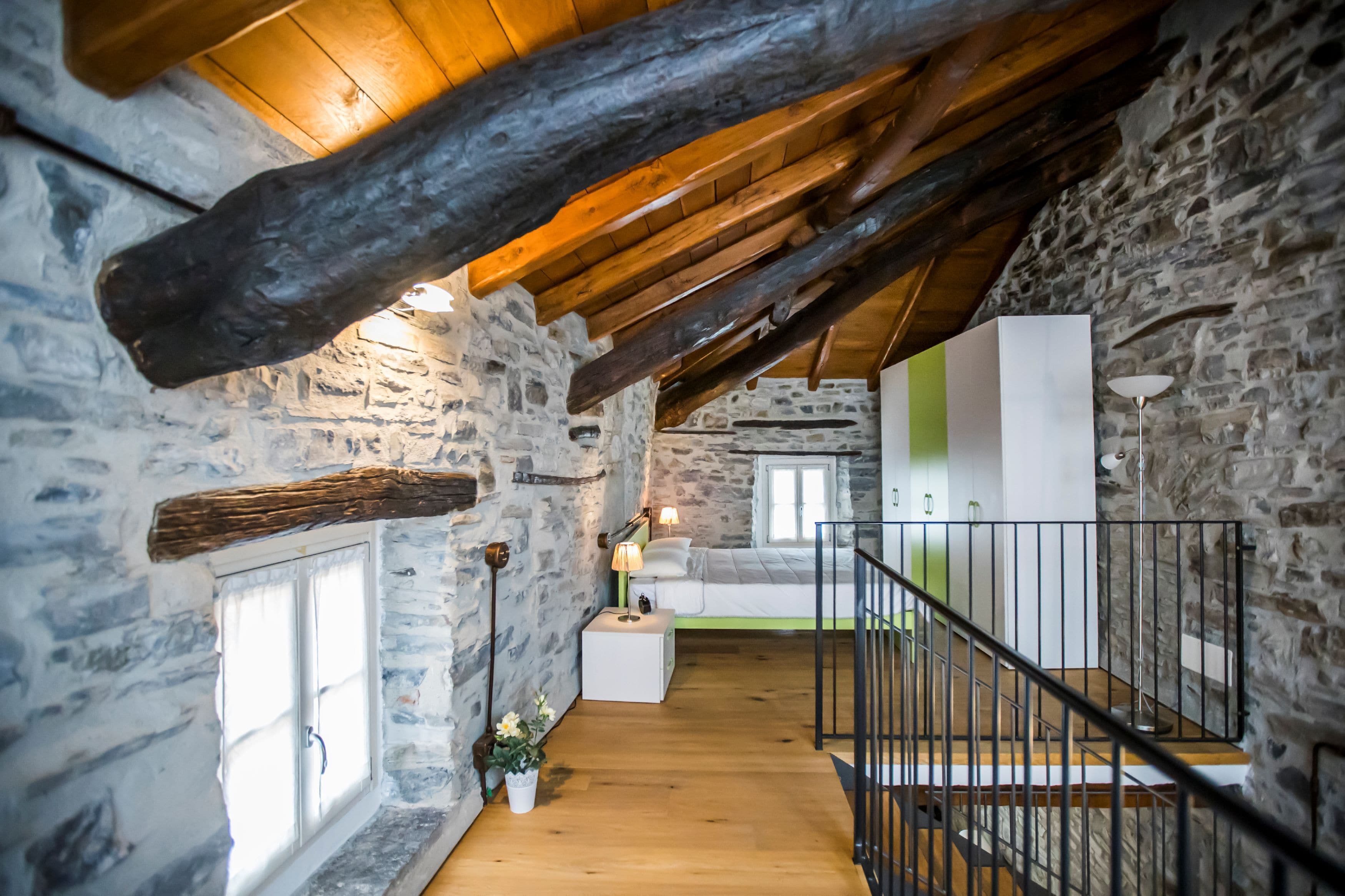 Interior rústico de piedra con vigas de madera, una escalera y un sofá blanco.