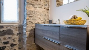 A room with a stone wall, wooden floor, a mirror, a sink, and a wooden cabinet.