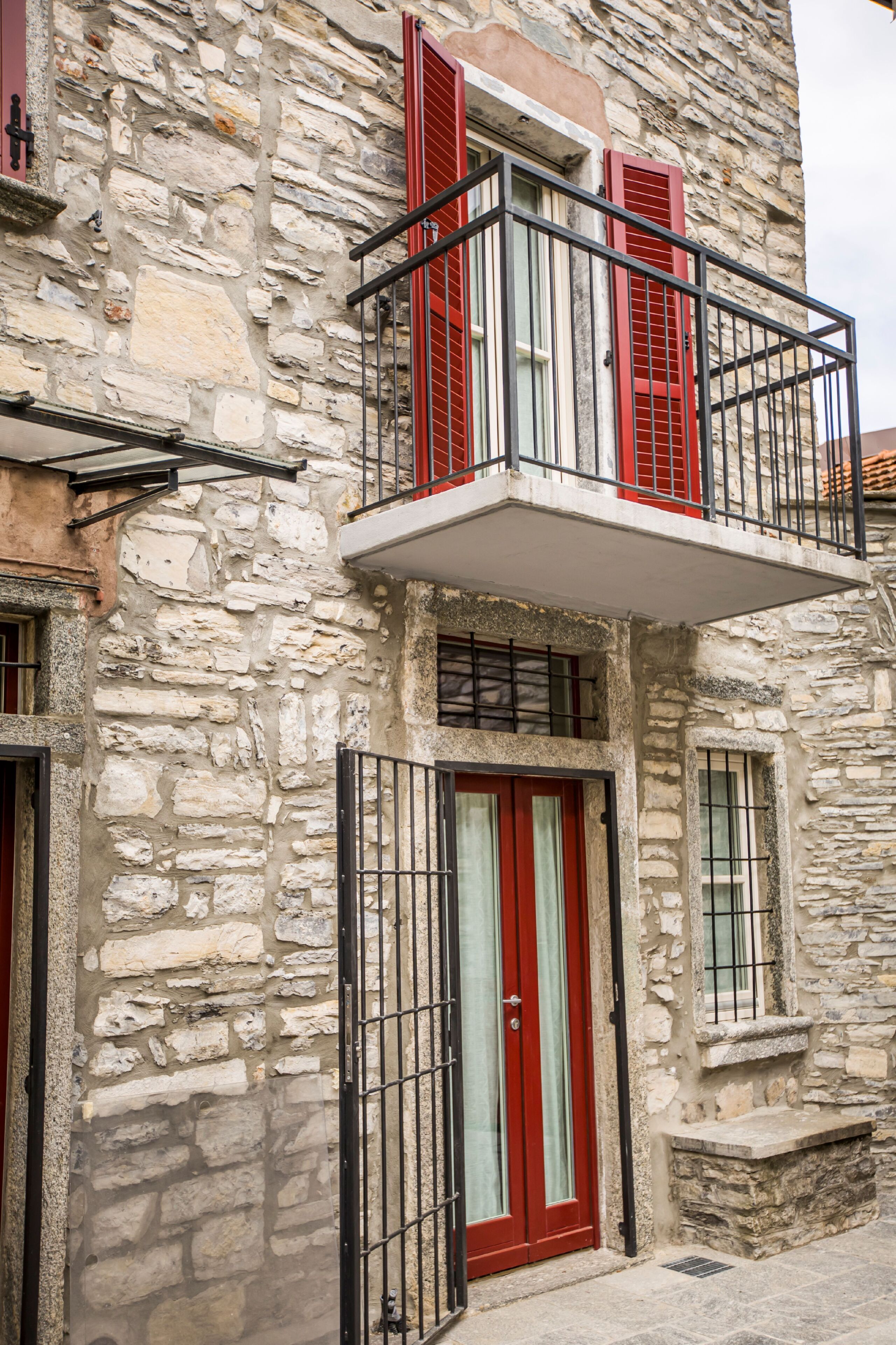 Ein Steinhaus mit Balkon, einer roten Tür und einem Fenster mit Metallgitter.