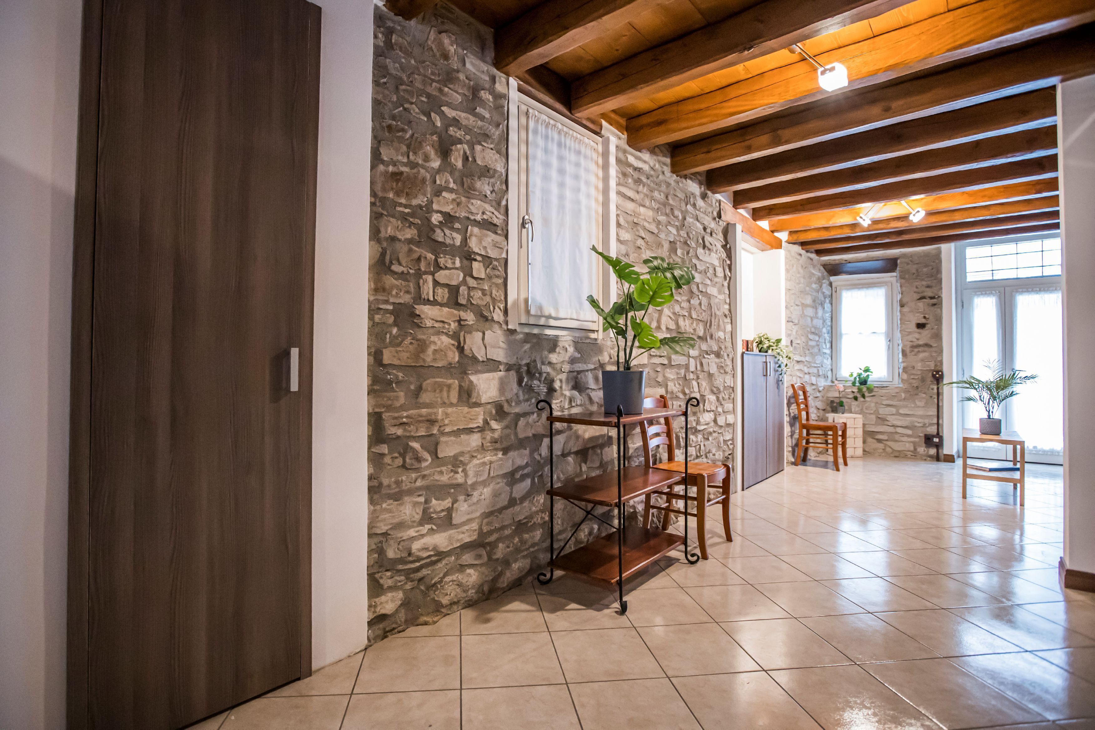 A room with stone walls, wooden ceiling beams, a tiled floor, and a wooden door.