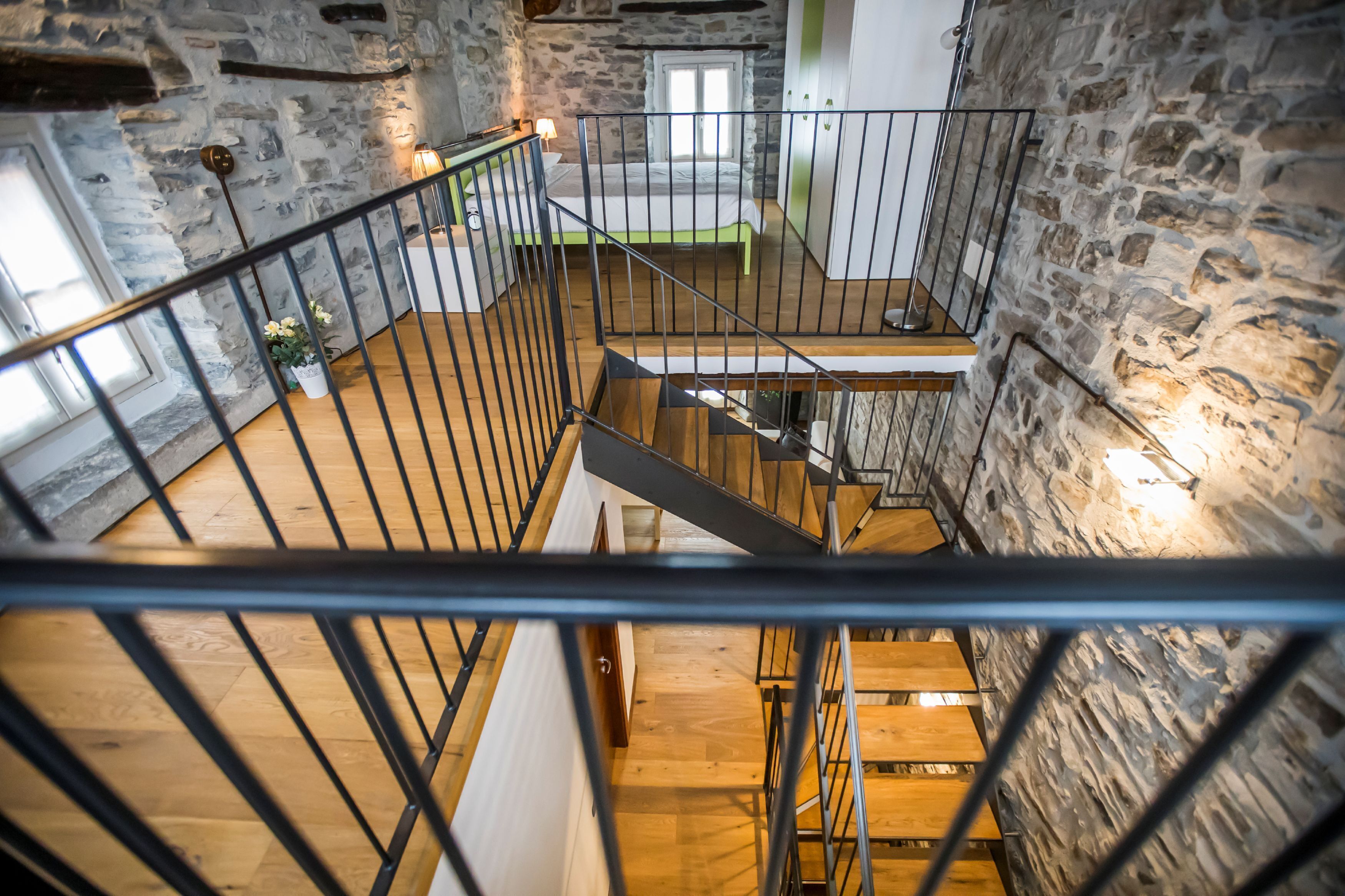 A multi-level interior with a staircase, stone walls, and a bed in the upper room.