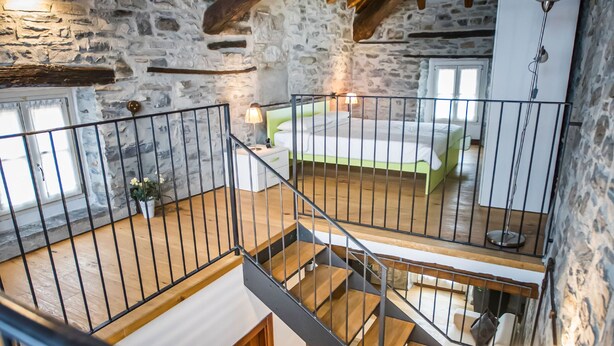 A multi-level wooden interior with stone walls, a staircase, and a bed.