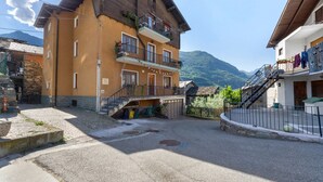 Un immeuble à plusieurs étages, doté de balcons, d’un escalier en pierre et offrant une vue sur les montagnes.