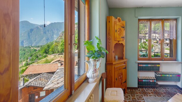 Une chambre avec vue sur les montagnes, un meuble en bois, un radiateur et une fenêtre ornée de rideaux en dentelle.