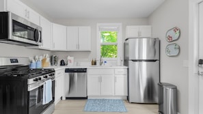 A modern kitchen with white cabinets, stainless steel appliances, and a window with a view of greenery.
