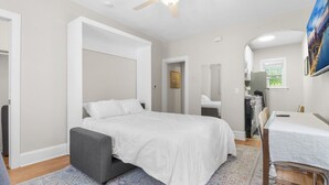 Une chambre à coucher avec un lit, un bureau, une chaise, un miroir et une fenêtre.