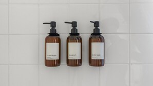 Trois flacons de produits de toilette sont posés sur un mur carrelé.