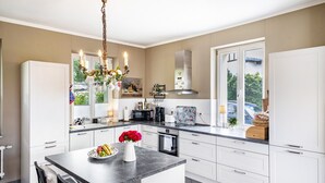 Cozinha moderna com armários brancos, bancada de mármore, lustre e vista para o exterior.