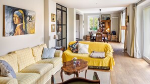 Uma sala de estar com um sofá amarelo, um sofá quadriculado, uma mesa de centro de madeira e uma pintura na parede.