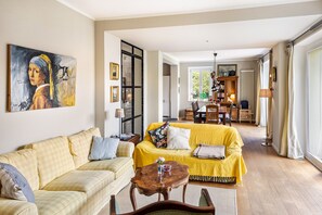 Una sala de estar con un sofá amarillo, un sofá a cuadros, una mesa de centro de madera y un cuadro en la pared.