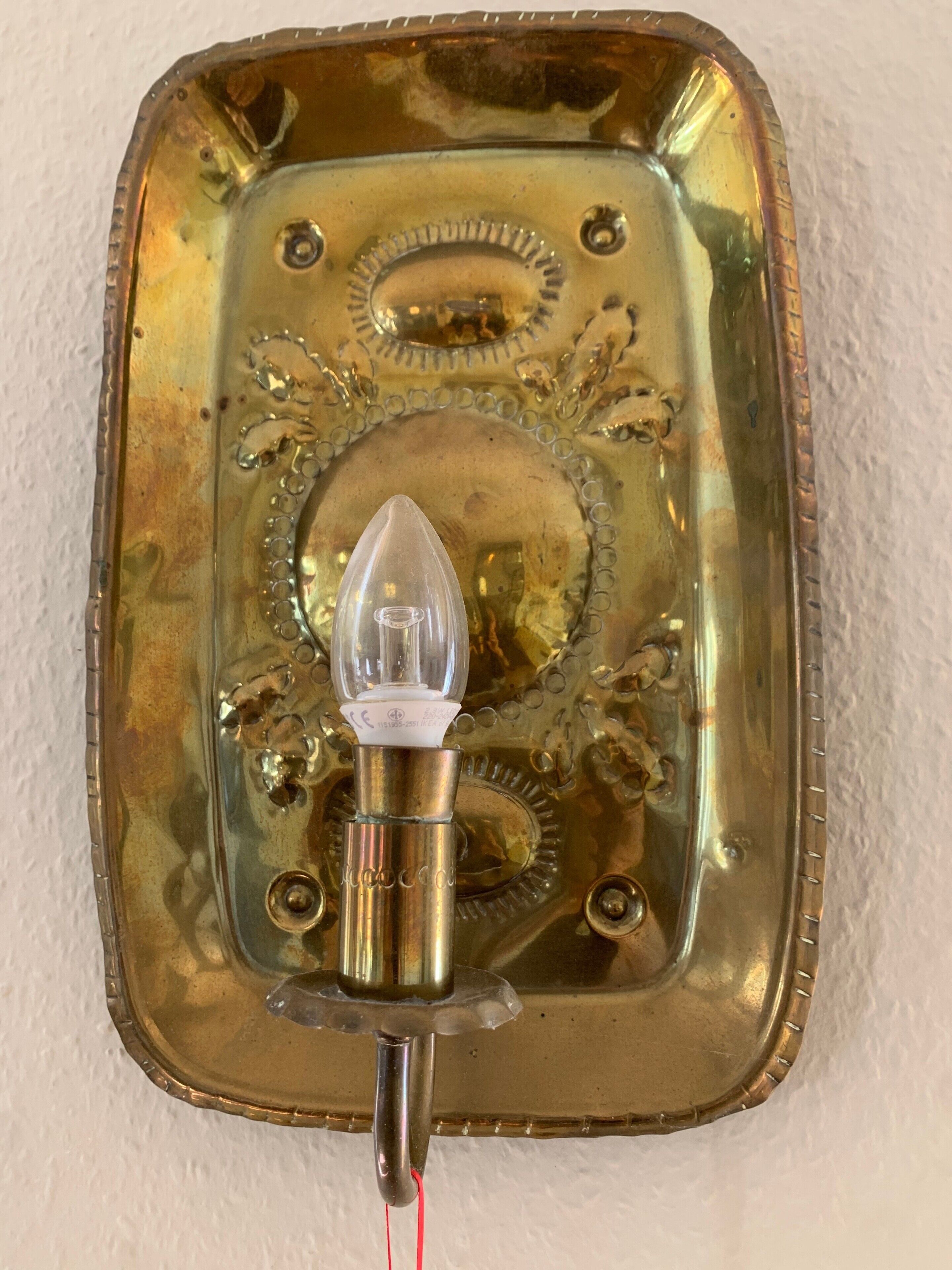 A brass wall-mounted light fixture with a clear glass bulb and decorative engravings.