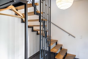 Una escalera con escalones de madera y barandas de metal, un perchero de madera y una lámpara colgante.