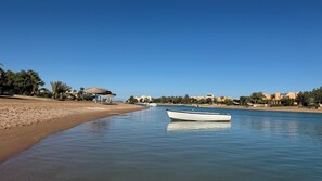 A calm river with a boat anchored near the shore, surrounded by palm trees and buildings.