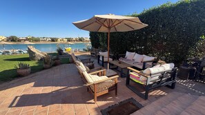 An outdoor patio with a table and chairs, a large umbrella, and a view of the sea.
