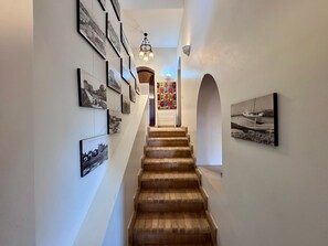 A staircase with a chandelier, framed photographs on the walls, and an archway leading to a room.