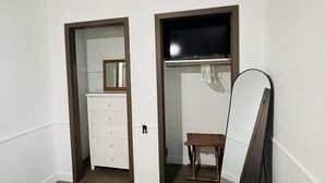 Ein Zimmer mit Holzboden, weißen Wänden, einem an der Wand angelehnten Spiegel und einer kleinen Holzbank.