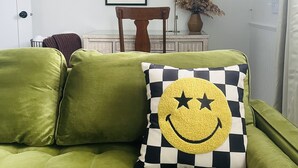 Ein grünes Sofa mit einem karierten Kissen, ein gerahmtes Bild an der Wand und eine Vase mit getrockneten Blumen.