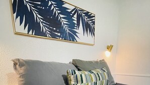 Ein Bett mit dunkelblauer Bettdecke, zwei Kissen, einer Wandleuchte und einem gerahmten Kunstwerk darüber.
