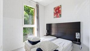 Ein Schlafzimmer mit zwei Betten, einem Fenster mit Vorhängen, einem Kopfteil, Nachttischlampen und einem Wandbild.
