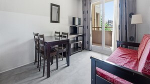 Ein Hotelzimmer mit Bett, Schreibtisch mit Stühlen, Fernseher und einem Balkon mit Vorhängen.