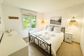 Ein Schlafzimmer mit Bett, Nachttischen, einem Schreibtisch und einem Fenster mit Blick ins Grüne.