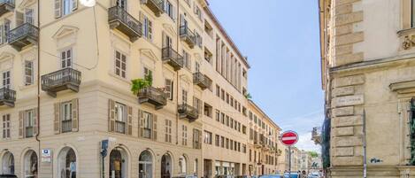 A street with parked cars, a no entry sign, and a building with balconies and arched windows.
