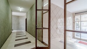 A hallway with a tiled floor, a glass door, and a view of the outside through a window. - GuestHost - Cozy Central Flat near Porta Nuova (Turin)