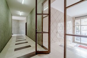 A hallway with a tiled floor, a glass door, and a view of the outside through a window. - GuestHost - Cozy Central Flat near Porta Nuova (Turin)