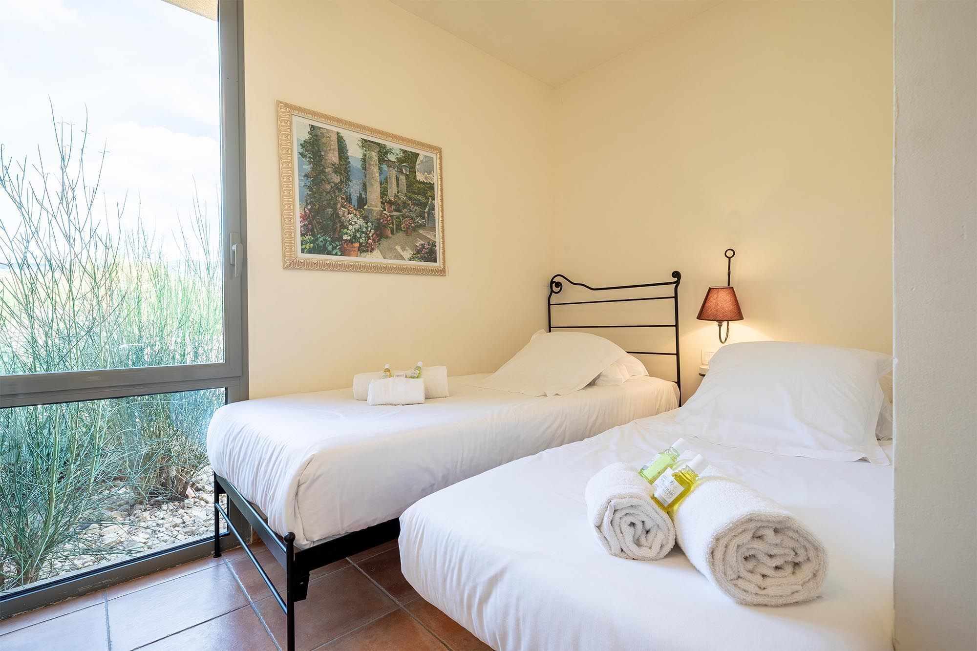 Une chambre avec deux lits, un tableau au mur, une fenêtre donnant sur un paysage verdoyant et une lampe sur la table de chevet.