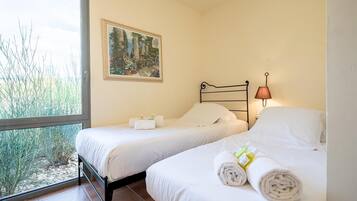 Une chambre avec deux lits, un tableau au mur, une fenêtre donnant sur un paysage verdoyant et une lampe sur la table de chevet.