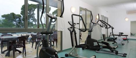 A gym with various exercise equipment, large windows, and a view of trees.