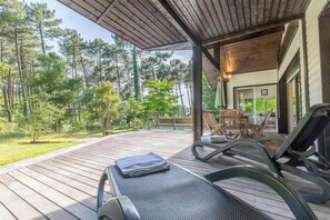 Eine überdachte Terrasse mit Liegestühlen, einem kleinen Tisch und einem Pool.
