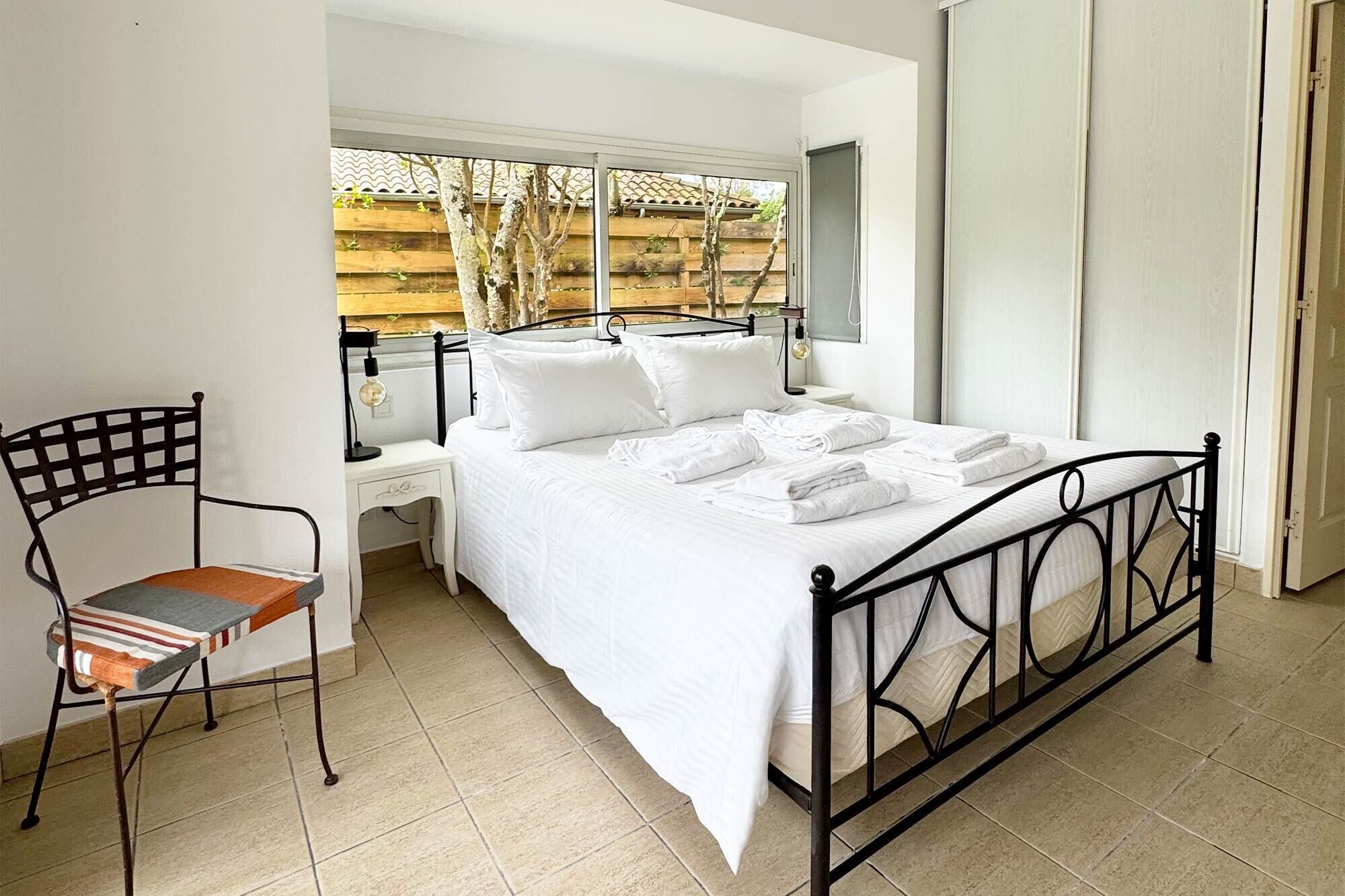 Une chambre à coucher comprenant un lit, une chaise, une table de chevet et une fenêtre donnant sur des arbres.