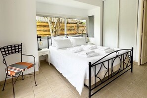 Ein Schlafzimmer mit Bett, Sessel, Nachttisch und Fenster mit Blick auf Bäume.