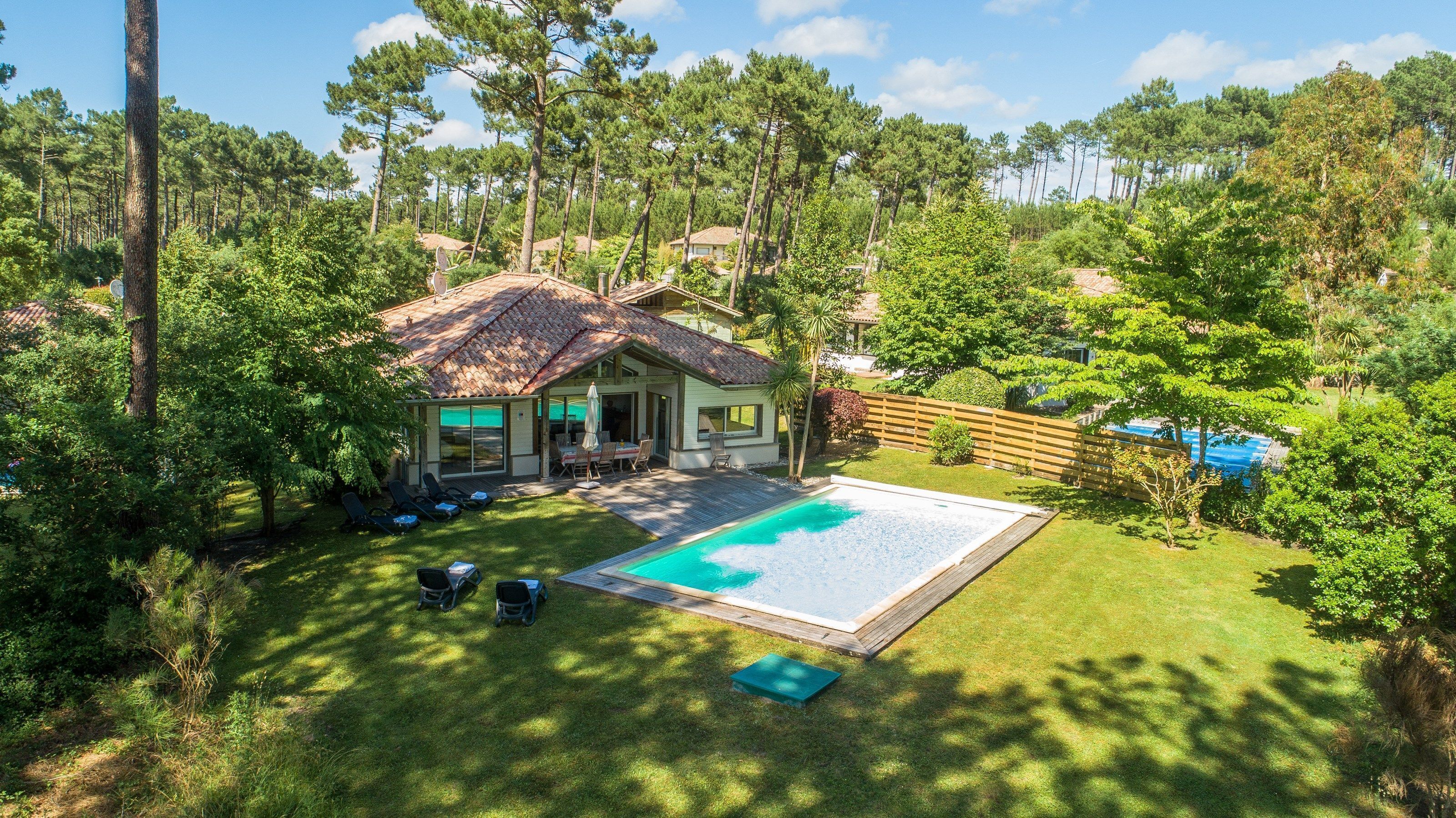 Una casa amb piscina envoltada per un terrat de fusta i un pati tancat per una tanca.