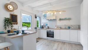 A modern kitchen with white cabinetry, a built-in oven, and a large window. - Holiday Home “Le Petit Baigneur” with Private Terrace, Shared Garden & Wi-Fi (Plouha)
