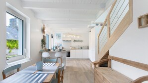 A modern kitchen with white cabinets, a wooden staircase, and a dining area with striped tablecloths. - Holiday Home “Le Petit Baigneur” with Private Terrace, Shared Garden & Wi-Fi (Plouha)