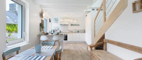 A modern kitchen with white cabinets, a wooden staircase, and a dining area with striped tablecloths.