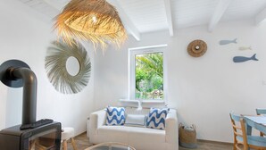 A cozy living room with a white sofa, a glass coffee table, a wooden dining table, and a wood-burning stove. - Holiday Home “Le Petit Baigneur” with Private Terrace, Shared Garden & Wi-Fi (Plouha)