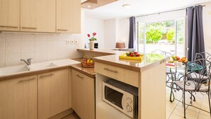 A modern kitchen with wooden cabinets, a built-in oven, a microwave, and a dining area with metal chairs. - French Riviera Bay Retreat (Arcachon)