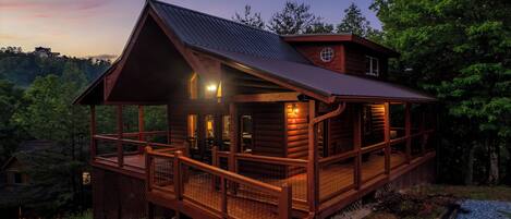 A log cabin with a balcony, a covered porch, and a metal roof.